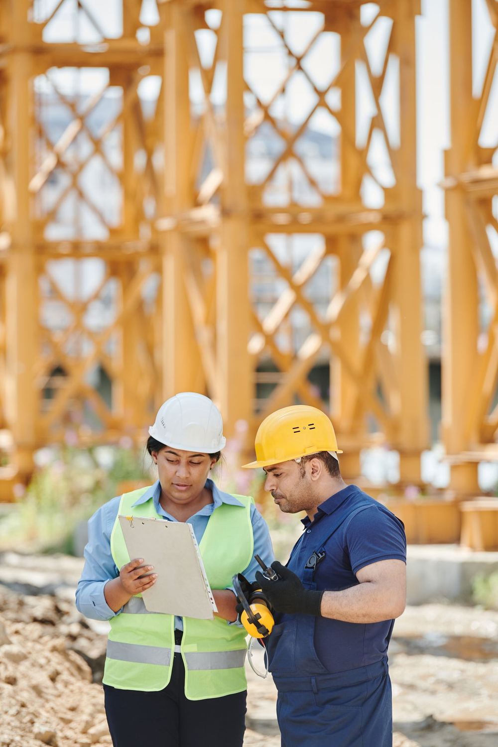 Two professionals in hard hats reviewing a document on a construction site